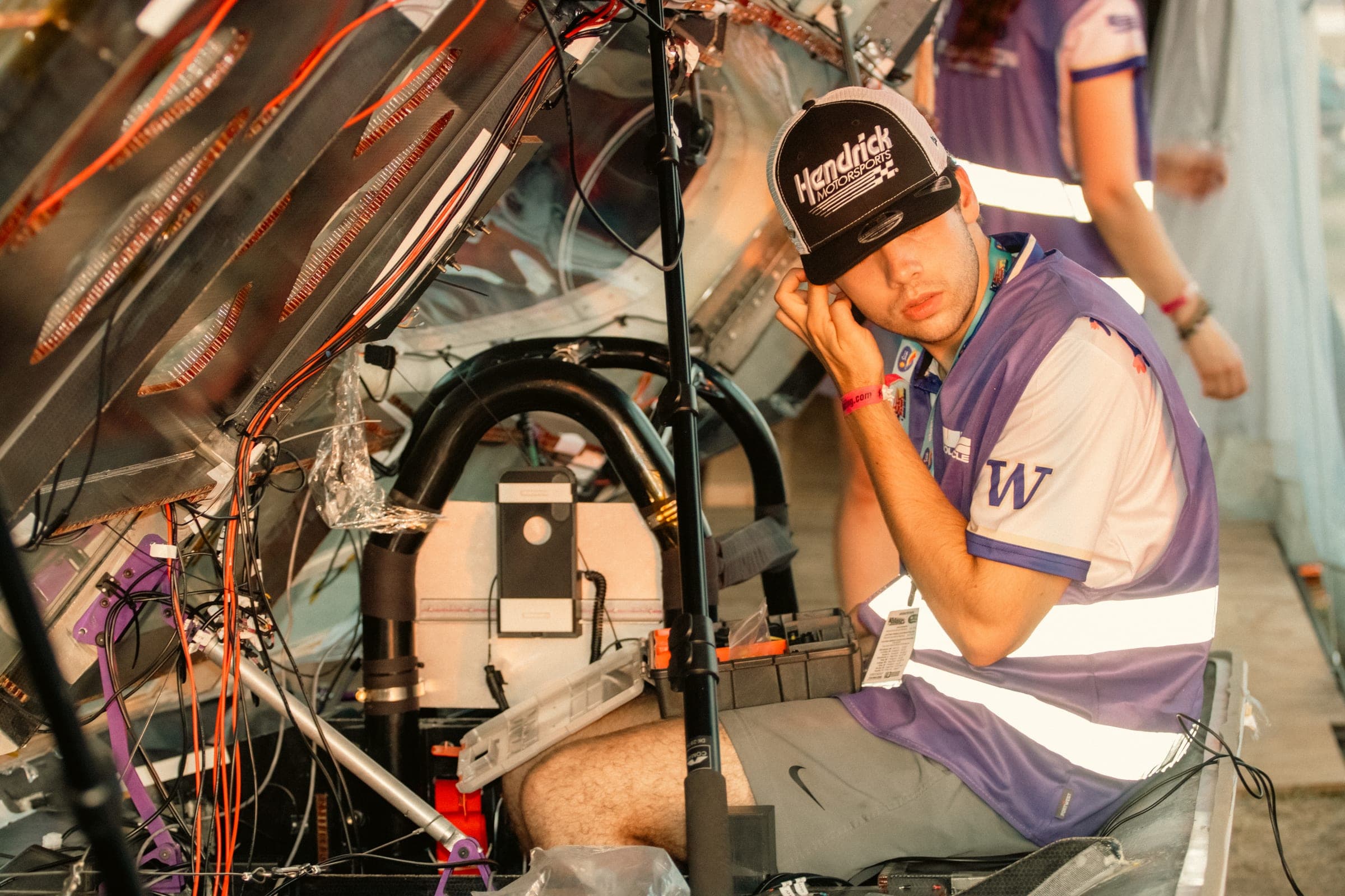 A team member working on the car's wiring and electronics under the raised shell